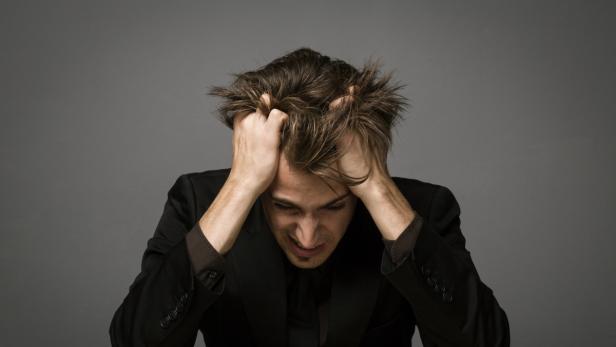 Ein verzweifelter Mann in einem Anzug fährt sich mit beiden Händen durch die Haare.