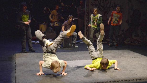 Zwei Jungen machen Breakdance auf einer Bühne, während eine Band im Hintergrund spielt.
