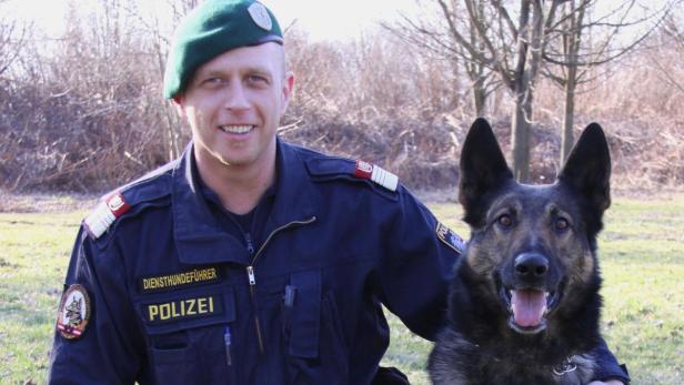 Ein lächelnder österreichischer Polizist mit Barett und Diensthund.