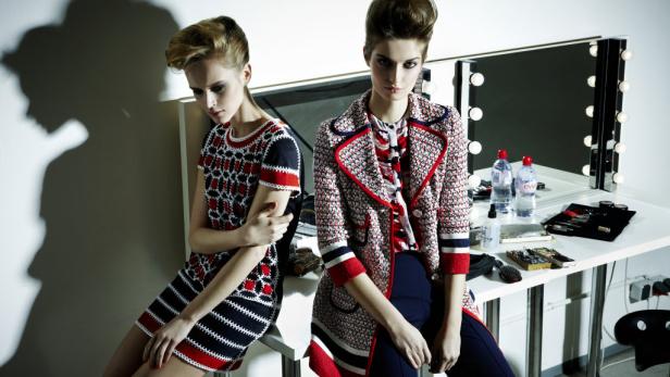 Zwei junge Frauen posieren in farbenfroher Kleidung vor einem Schminktisch mit Spiegel.