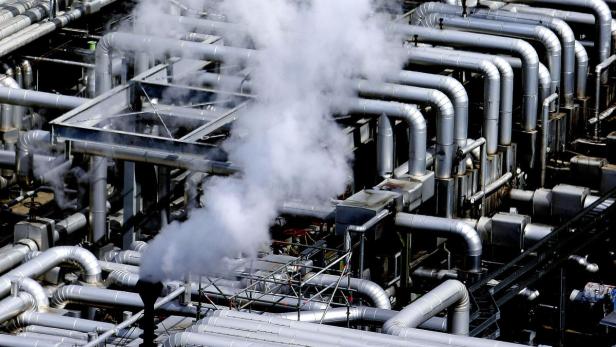 Ein komplexes Netzwerk von Rohren in einer Industrieanlage mit aufsteigendem Dampf.