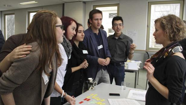 Eine Gruppe junger Leute steht um einen Tisch und diskutiert angeregt.