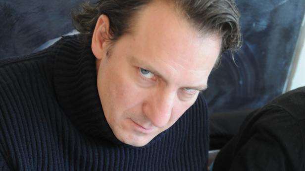 Ein Mann mit blauen Augen und einem schwarzen Rollkragenpullover blickt in die Kamera.