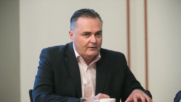 Ein Mann in Anzug und Hemd sitzt an einem Tisch.