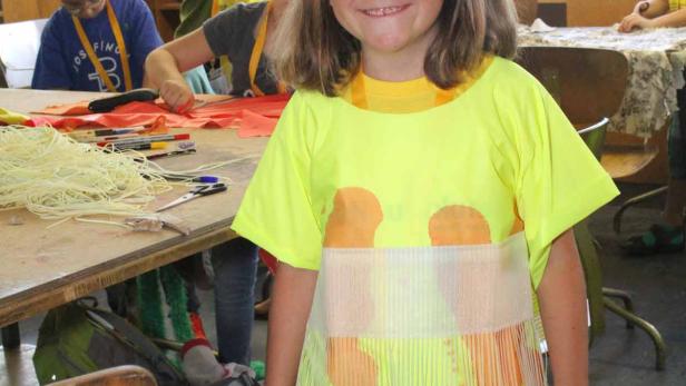 Ein Mädchen mit einem Kostüm und einem blauen Hut auf dem Kopf lächelt.