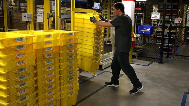 Ein Arbeiter in einem Lagerhaus bewegt einen Stapel gelber Behälter.
