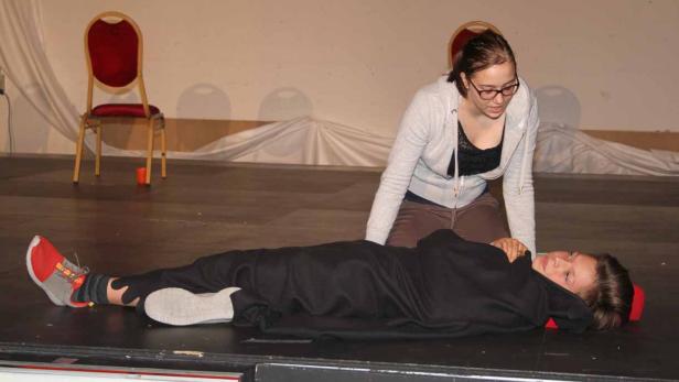 Eine junge Frau kniet neben einer anderen Person, die auf einer Bühne liegt.