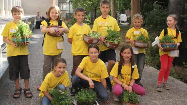 Eine Gruppe Kinder in gelben T-Shirts präsentiert bepflanzte Töpfe.