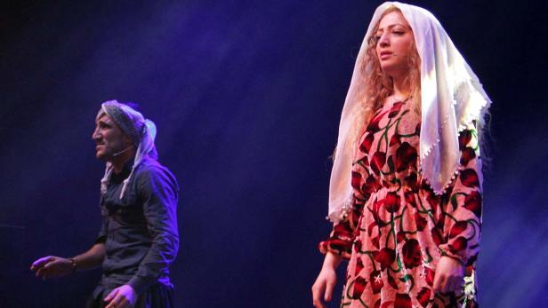 Zwei Schauspieler in traditionellen Kostümen stehen auf einer Bühne.