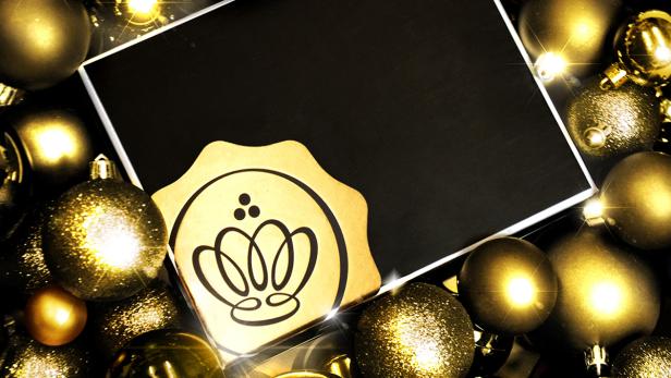 Goldene Weihnachtskugeln umrahmen eine schwarze Fläche mit einem goldenen Siegel.