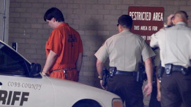 Ein Gefangener in oranger Kleidung wird von Polizisten des Cobb County Sheriff begleitet.