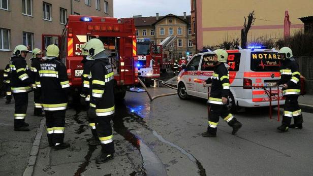 Feuerwehrleute und Einsatzfahrzeuge stehen auf einer nassen Straße.