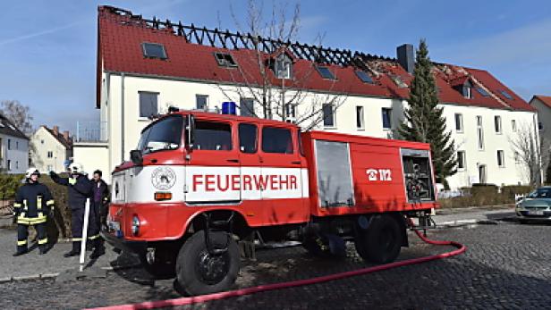 Ein rotes Feuerwehrfahrzeug steht vor einem Gebäude mit Brandschaden am Dach.