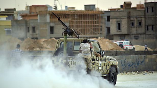 Ein Militärfahrzeug mit montiertem Maschinengewehr fährt durch eine staubige Straße.