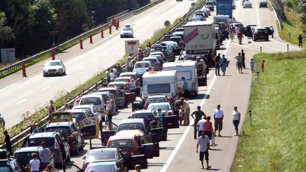 Auf einer Autobahn stehen viele Autos im Stau, einige Menschen stehen davor.