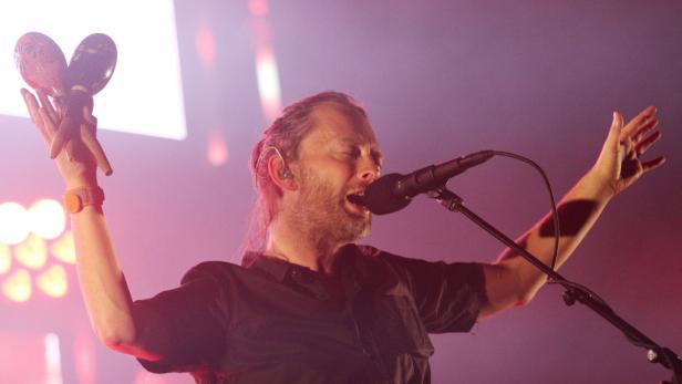 Thom Yorke von Radiohead singt mit Maracas in der Hand auf der Bühne.
