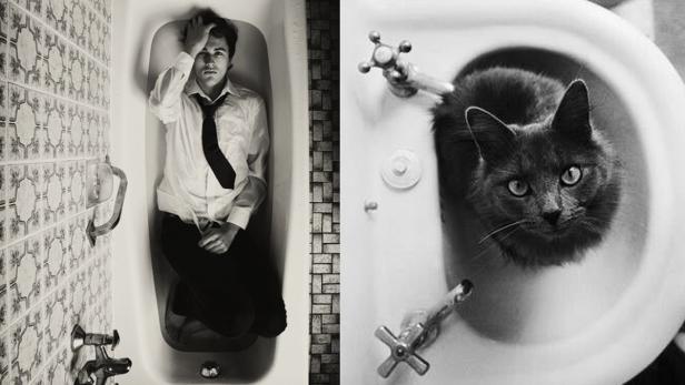 Ein Mann liegt in einer Badewanne, während eine Katze in einem Waschbecken sitzt.