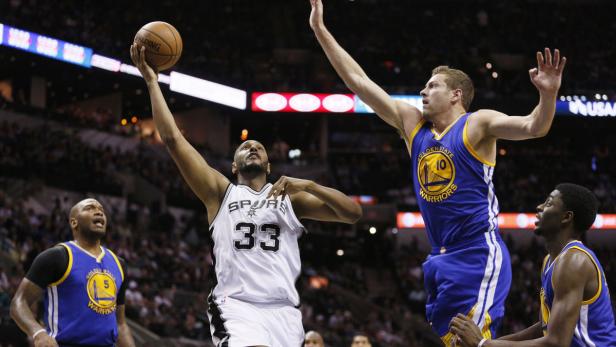 Ein Basketballspieler der Spurs wirft den Ball, während ein Spieler der Golden State Warriors ihn verteidigt.