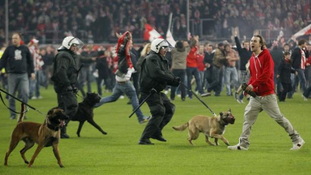 Polizisten mit Hunden räumen ein Fußballfeld voller Fans.