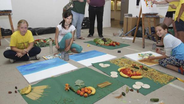 Mehrere Kinder malen und gestalten Bilder mit Lebensmitteln auf dem Boden.