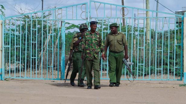 Drei bewaffnete Sicherheitskräfte gehen durch ein blaues Tor.