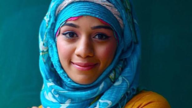 Eine junge Frau mit einem blauen Hijab lächelt in die Kamera.