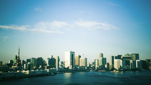 Die Skyline von Tokio erstreckt sich entlang des Wassers unter einem hellblauen Himmel.