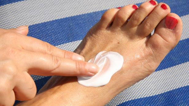 Eine Person cremt ihren Fuß mit Sonnencreme ein.