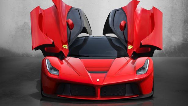 Ein roter Ferrari mit geöffneten Flügeltüren steht vor einer grauen Wand.