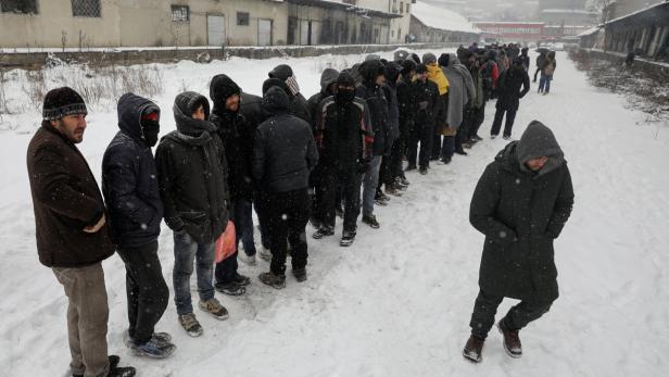 Eine lange Schlange von Menschen steht im Schnee vor einem Gebäude.