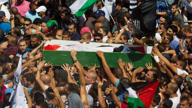 Eine Menschenmenge trägt einen Sarg, der mit der palästinensischen Flagge bedeckt ist.