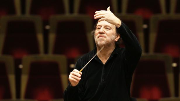 Ein Dirigent mit erhobenem Taktstock vor einem Orchester.