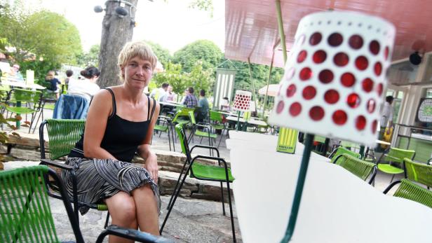 Eine Frau sitzt in einem Straßencafé mit grünen Stühlen.