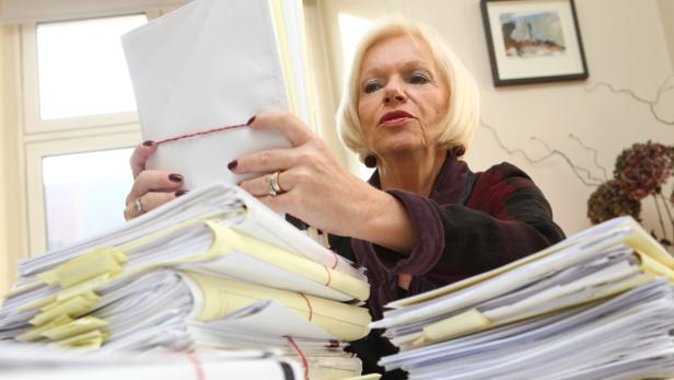 Eine Frau mit blonden Haaren sortiert Papierstapel auf einem Schreibtisch.