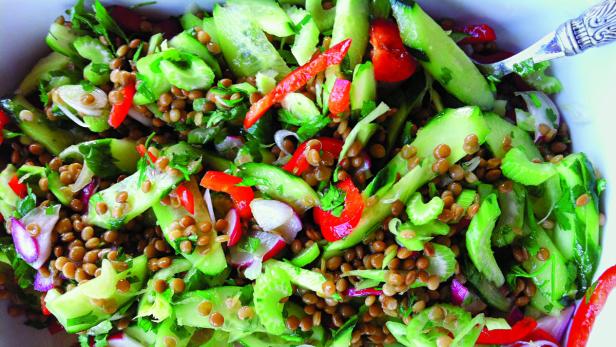 Ein Linsensalat mit Gurken, Radieschen, Paprika und Kräutern wird mit einem Löffel serviert.