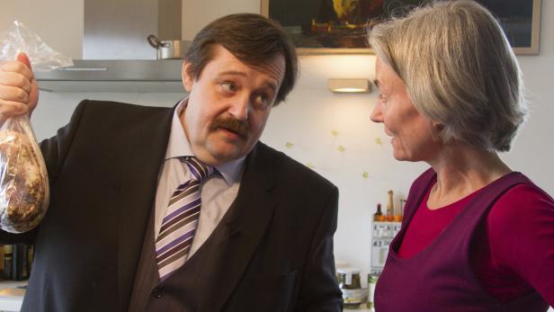 Ein Mann im Anzug zeigt einer Frau einen Beutel mit Fleisch.