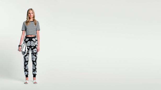 Eine Frau mit blonden Haaren trägt ein gestreiftes Oberteil und eine Hose mit Blumenmuster.