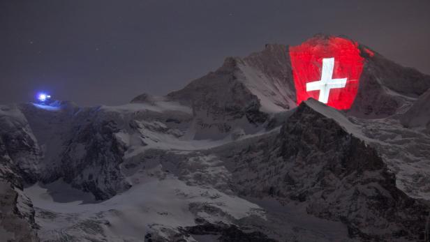 Die Schweizer Flagge wird nachts auf einen schneebedeckten Berg projiziert.