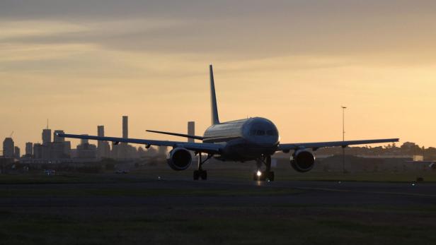 Ein Flugzeug landet bei Sonnenuntergang auf einer Landebahn vor einer Stadtkulisse.
