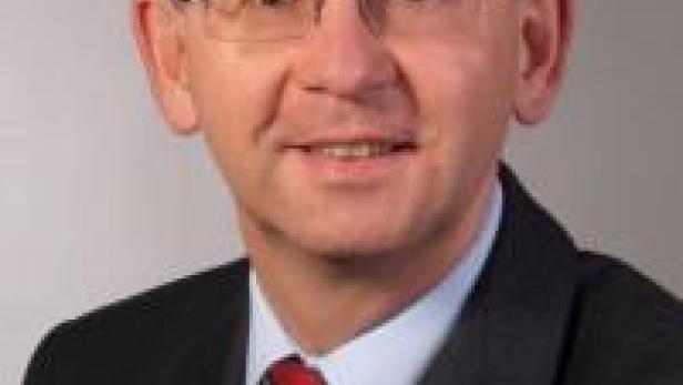 Ein Mann mit Brille, Anzug und Krawatte lächelt in die Kamera.