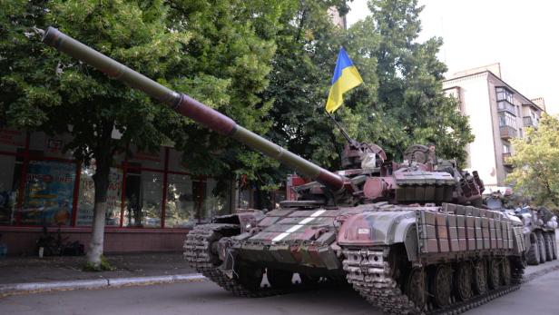Ein Panzer mit ukrainischer Flagge steht auf einer Straße.