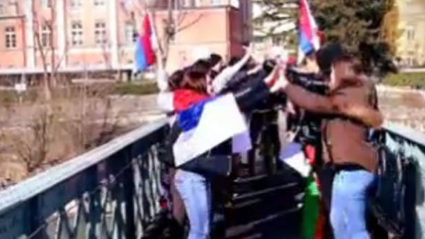 Eine Gruppe von Menschen steht auf einer Brücke und hält Fahnen hoch.