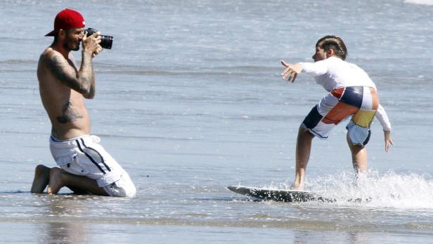 Ein Mann fotografiert einen Jungen, der auf einem Surfbrett im Wasser steht.