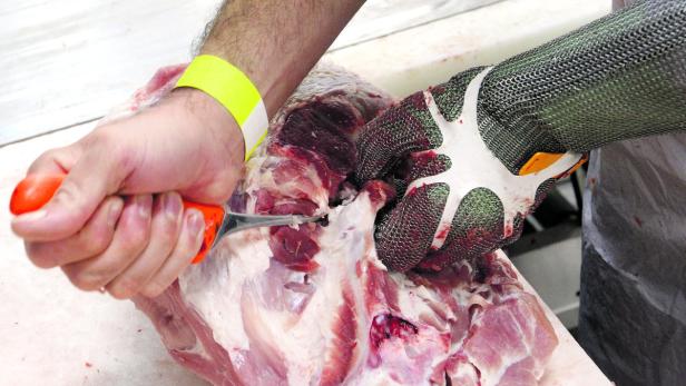 Ein Metzger zerlegt ein Stück Fleisch mit einem Messer und trägt dabei einen Kettenhandschuh.