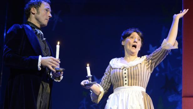 Zwei Schauspieler stehen mit Kerzen in der Hand auf einer Bühne.