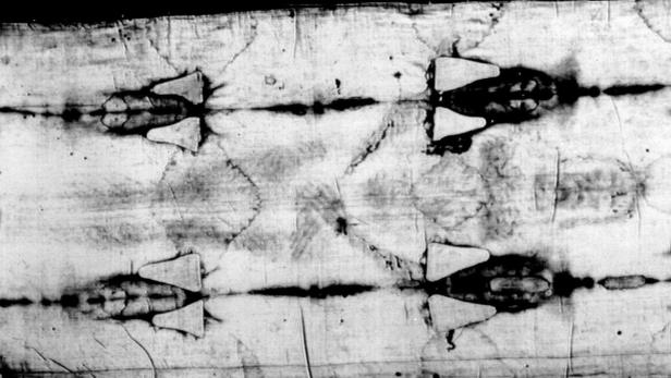 Detailaufnahme des Turiner Grabtuchs mit dunklen Flecken und geometrischen Mustern.