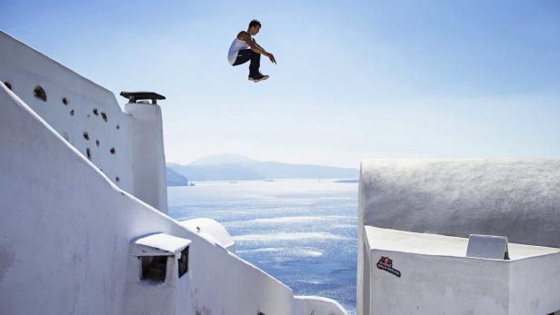 Ein Mann springt über weiße Gebäude mit dem Meer im Hintergrund.