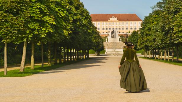 Eine Frau in historischer Kleidung geht auf das Schloss Schönbrunn zu.