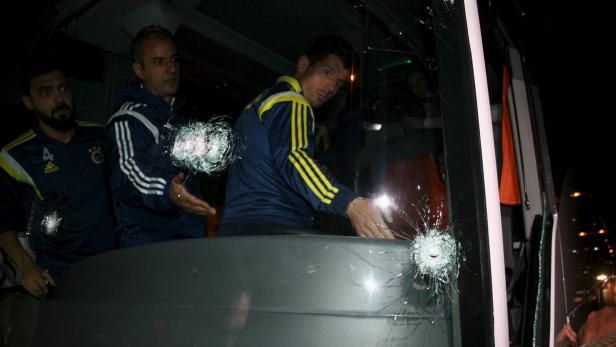 Ein Bus mit eingeschossenen Fenstern und drei Männern in Sportkleidung darin.