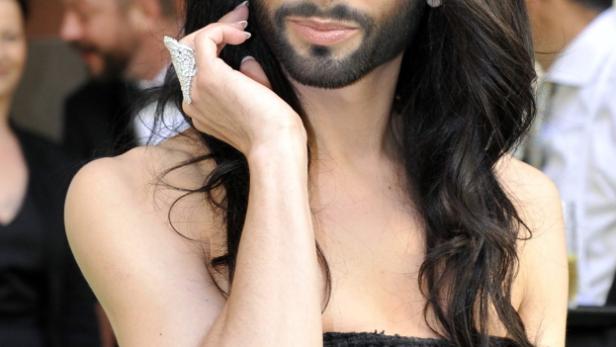 Conchita Wurst posiert in einem schwarzen Kleid mit einem auffälligen Ring.
